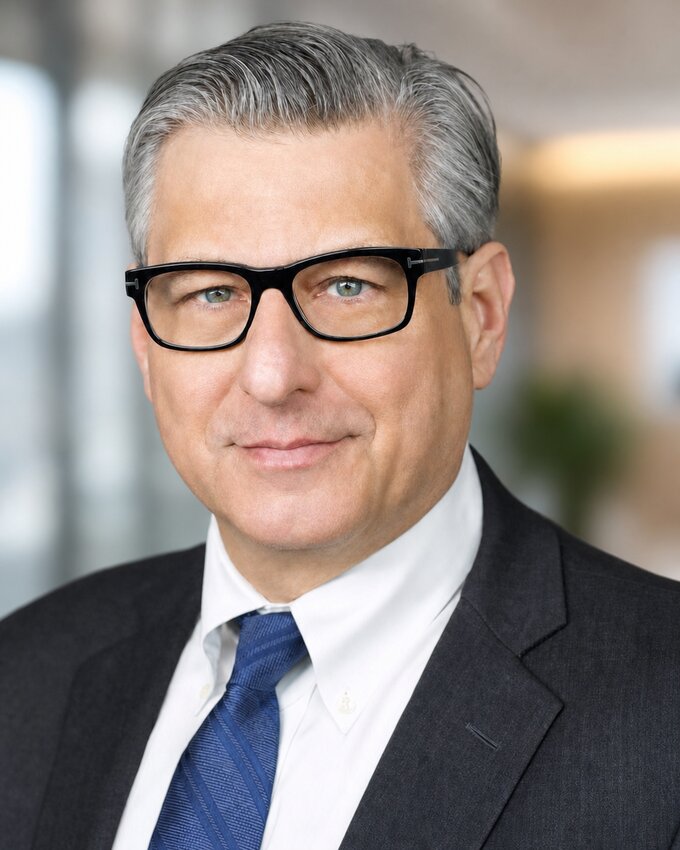 Corporate headshot of a man in glasses with a blurred office background, NYC